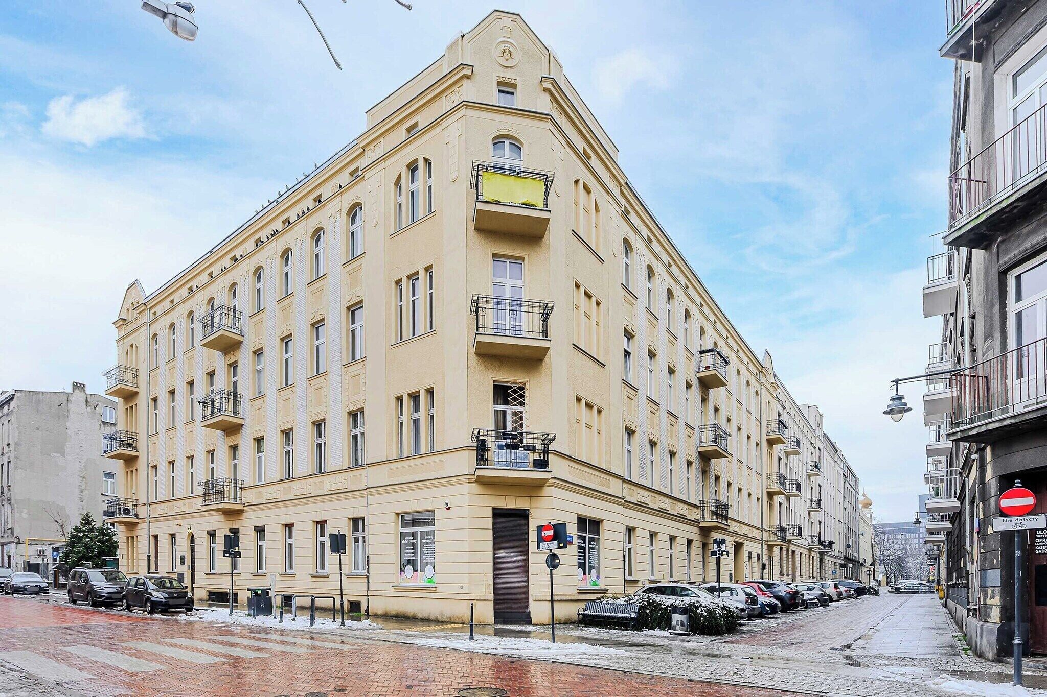 Un edificio de varios pisos con entrada en esquina, varios balcones y acceso visible en la planta baja.