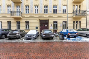 A row of parked cars in front of a building with a brick facade and a large door. - Apartment near Moniuszko Park (Łódź)