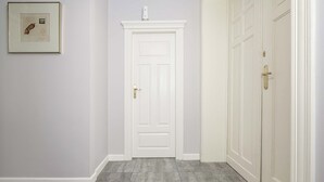 Ein Flur mit einer weißen Tür, einem gerahmten Bild an der Wand und einer Reihe weißer Türen rechts.