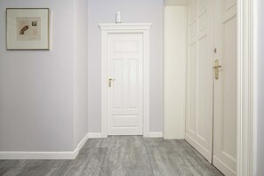 Ein Flur mit einer weißen Tür, einem gerahmten Bild an der Wand und einer Reihe weißer Türen rechts.