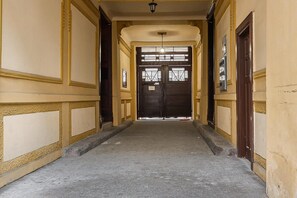 Un couloir se termine par une porte à deux battants, qui donne sur une pièce.