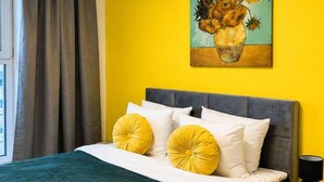 A bed with a grey headboard, white and yellow pillows, and a teal bedspread. There are two wine glasses on the bed. - Modern Romantic CIty Getaway (Łódź)