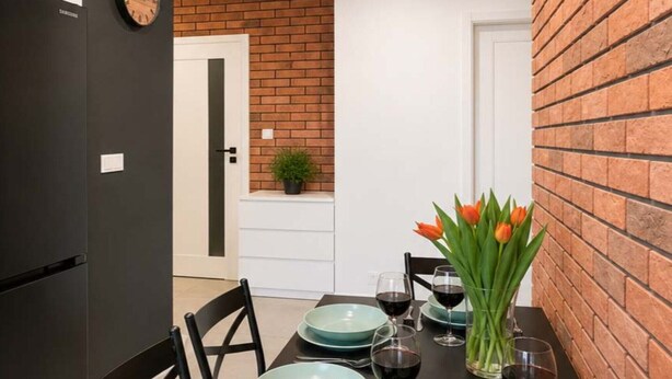 A dining area with a brick wall, a clock, and a table set with plates, glasses, and a vase of tulips. - Modern Romantic CIty Getaway (Łódź)