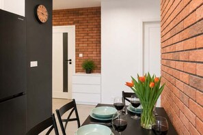 A dining area with a brick wall, a clock, and a table set with plates, glasses, and a vase of tulips. - Modern Family Getaway in Łódź  CIty (Łódź)