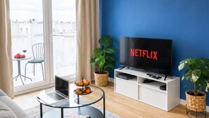 A modern living room with a large flat-screen TV, a laptop, a small round table with pastries, and a view of the city through a large window. - Modern Romantic CIty Getaway (Łódź)