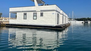 Ein feststehendes Hausboot mit flachem Dach, Fenstern und einer kleinen Deckfläche.