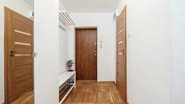 A narrow hallway with wooden flooring, a central door, and a small shelf with a plant. - Stay in Warsaw Center (Warszawa)