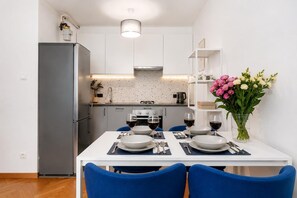 A modern kitchen with white cabinets, a grey refrigerator, and a dining area with a white table set for two. - Stay in Warsaw Center (Warszawa)