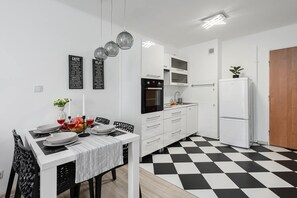 Eine moderne Küche mit Schachbrettboden in Schwarz und Weiß, weißen Schränken und einem Essbereich mit Tisch für vier Personen.