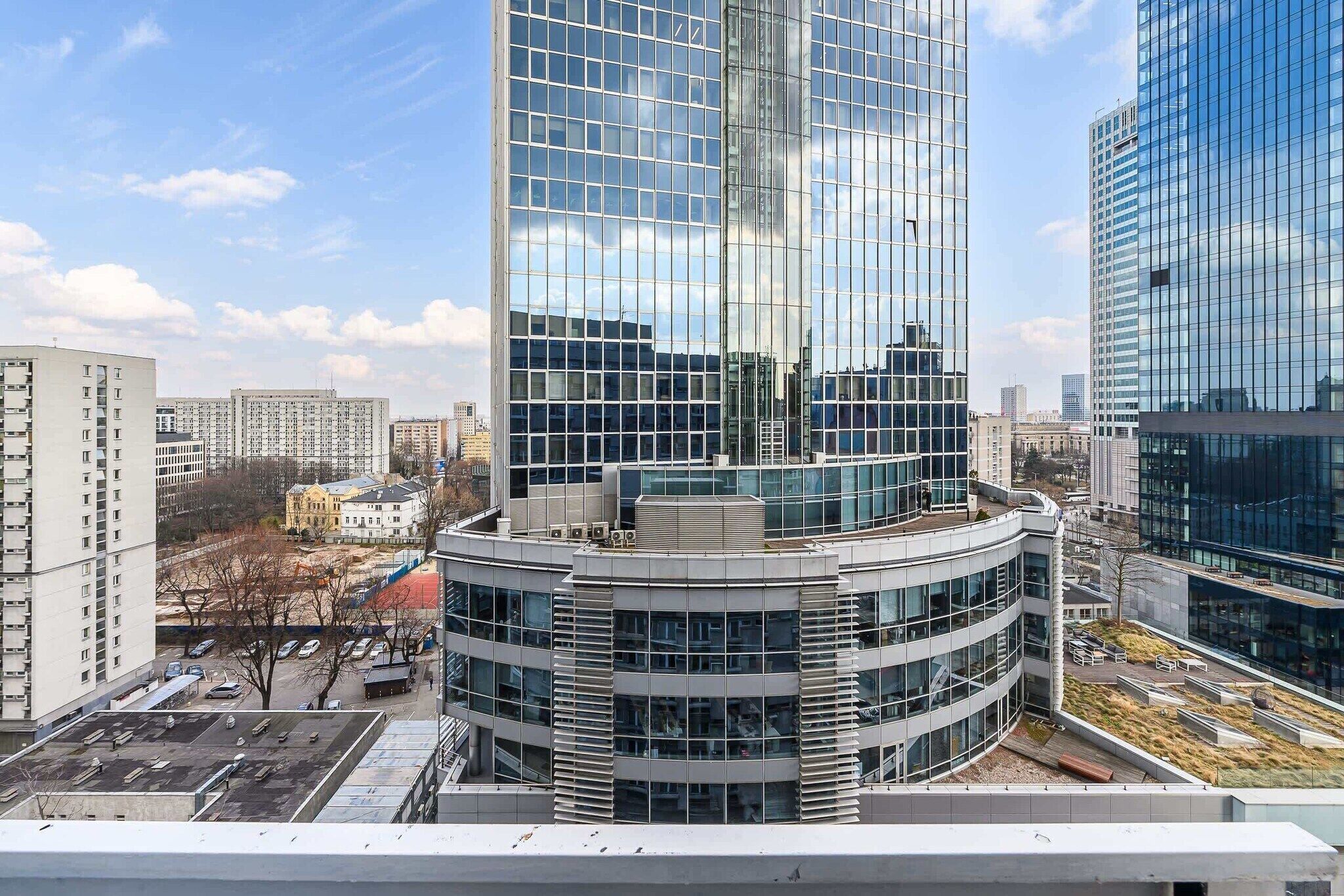A modern high-rise building with a curved glass facade, surrounded by other high-rise buildings in an urban setting.