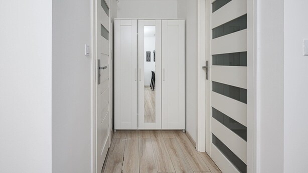 Un corridoio stretto con pareti bianche e pavimento in legno, che conduce a una porta con un pannello di vetro.