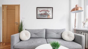 Ein modernes Wohnzimmer mit einem grauen Sofa, zwei Zierkissen, einem weißen Couchtisch, einer Topfpflanze und einem gerahmten Bild an der Wand.