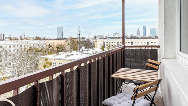 Ein Balkon mit Tisch und Stühlen mit Blick auf eine Stadtlandschaft mit Gebäuden und Bäumen.