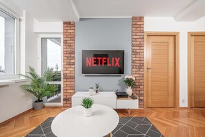 A modern living room with a flat-screen TV mounted on a brick wall, a white console table, a round coffee table, and a door with a wooden frame. - Cozy Apartment for 6 near VIstula River (Warszawa 2)