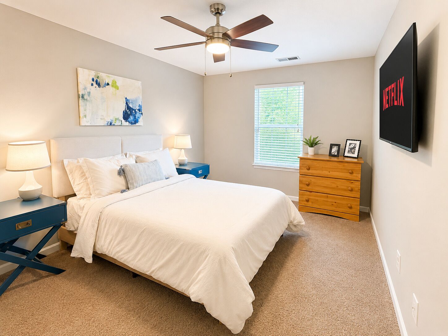 Ein Schlafzimmer mit Bett, Nachttischen, einem Schminktisch, einem Deckenventilator, einem Fenster mit Jalousien und einem an der Wand befestigten Fernseher.