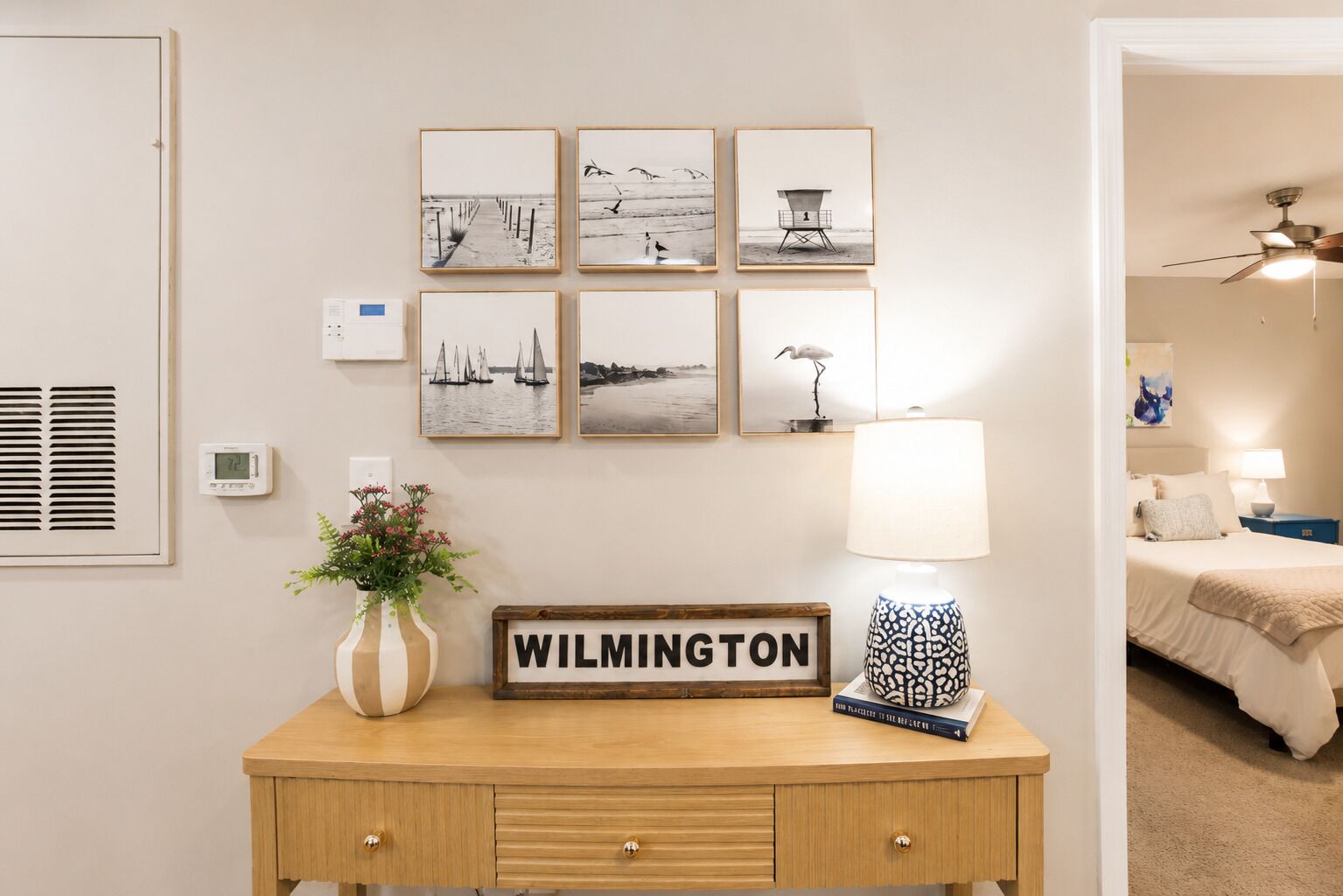 A hotel room with a bed, a bedside table with a lamp, a wall clock, and a series of framed pictures.