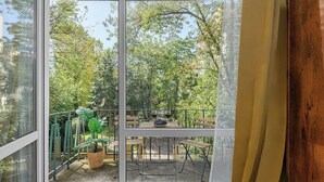 A balcony with a table and chairs, a potted plant, and a view of trees and buildings. - Lush Flat in Lodz Center (Łódź)