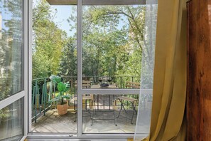 Ein Balkon mit Tisch und Stühlen, einem Blumentopf und Blick auf Bäume und Gebäude.