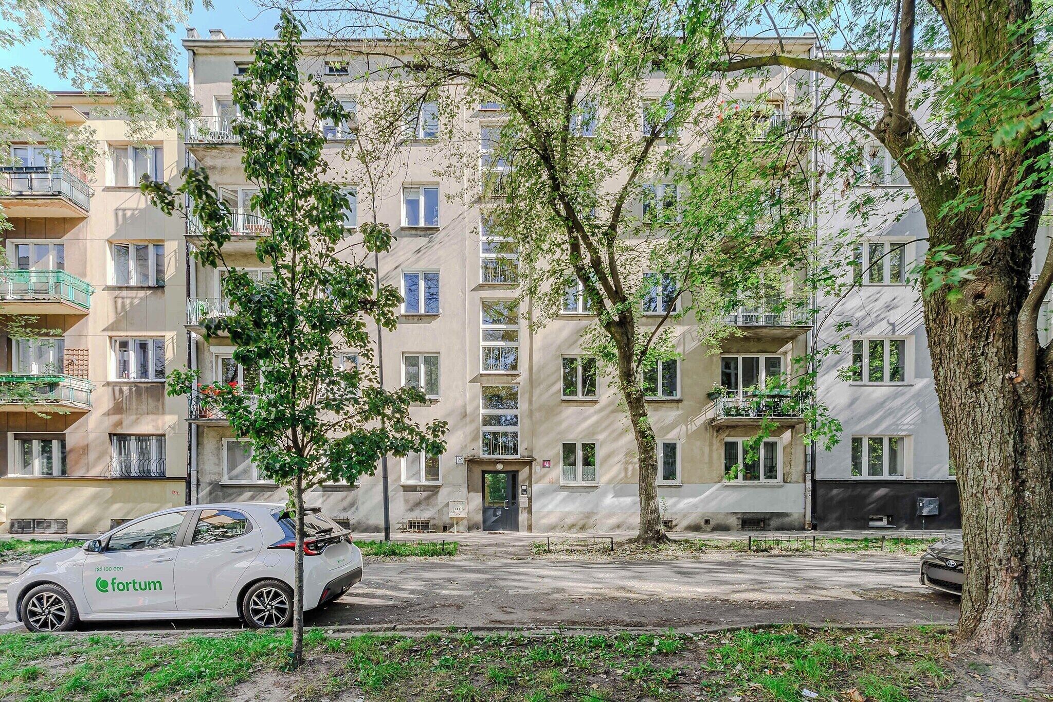 Un edificio residencial con varios balcones, un árbol en primer plano y un coche estacionado.