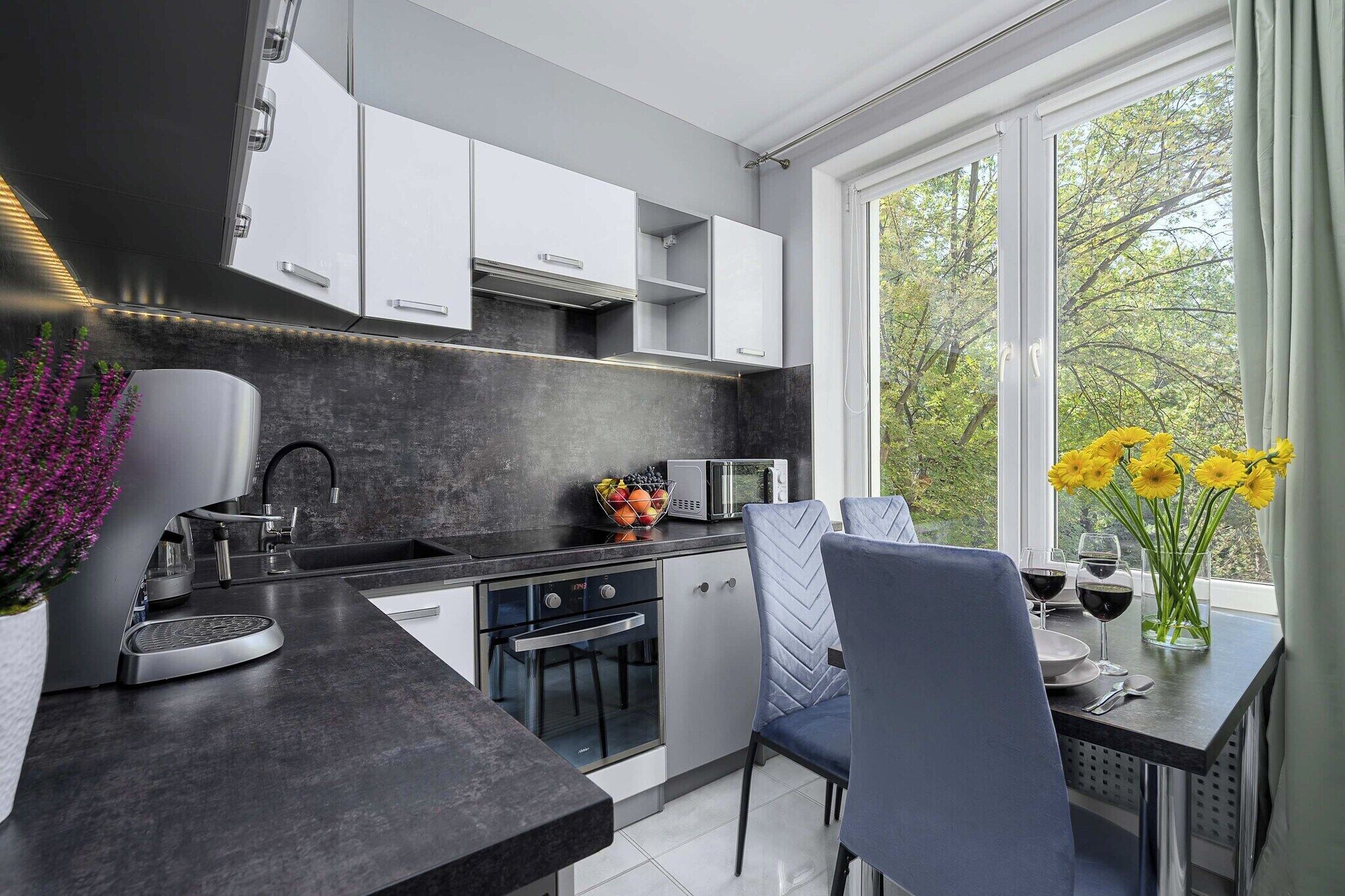 Una cocina moderna con armarios blancos, una encimera negra y un comedor con mesa y sillas.