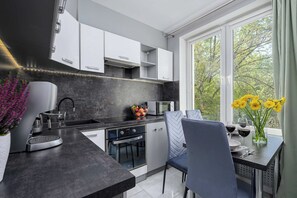 A modern kitchen with white cabinets, a black countertop, and a dining area with a table and chairs. - Lush Flat in Lodz Center (Łódź)