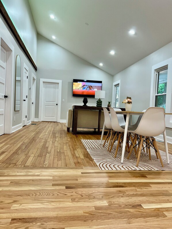 A modern dining area with a wooden floor, a television mounted on the wall, and a dining table with chairs. - The Carter Home 3Beds-2Ba-2Tvs minutes way to Lakepoint Sports (Cartersville)