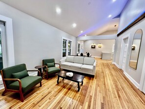 Un vaste espace de vie doté d’un plancher en bois, d’un canapé, de deux fauteuils et d’une table basse.