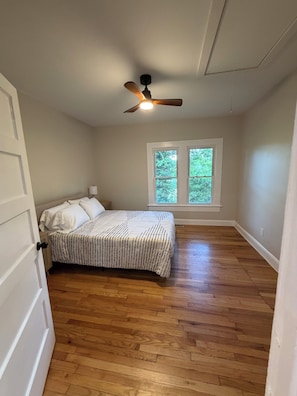 A bedroom with a bed, wooden flooring, a ceiling fan, and a window with a view of trees. - The Carter Home 3Beds-2Ba-2Tvs minutes way to Lakepoint Sports (Cartersville)