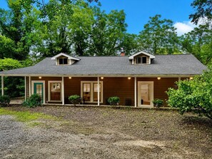 A two-story wooden house with a covered porch, a small attic window, and a gravel driveway. - The Carter Home 3Beds-2Ba-2Tvs minutes way to Lakepoint Sports (Cartersville)