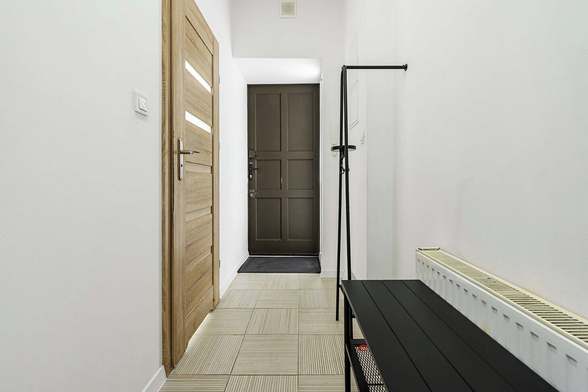 A hallway with a wooden door, a black bench, and a radiator.
