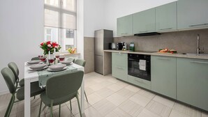 A modern kitchen with a dining area, featuring a table set for two, a refrigerator, an oven, and a microwave. - Holiday Home in Porspoder near Plage du Bourg (Łódź)