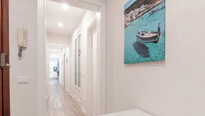 Un corridoio con una porta che conduce a una stanza, un quadro raffigurante una scena costiera e una panca.