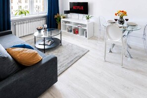 A modern living room with a sofa, coffee table, dining table, and a TV displaying 'NETFLIX'. - Elegant Apartment near Vitsula River (Warszawa)
