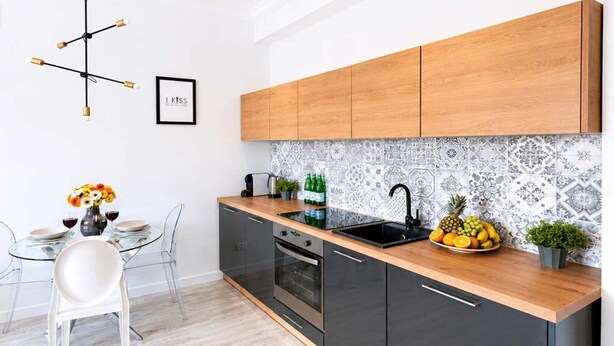 A modern kitchen with black cabinets, a wooden countertop, and a patterned backsplash. - Elegant Apartment near Vitsula River (Warszawa)