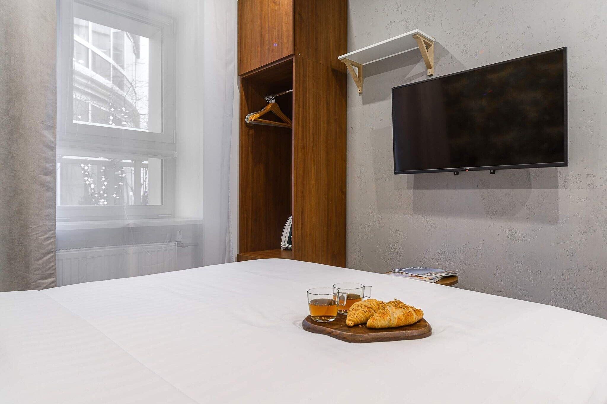 Una camera d'albergo con un letto, una televisione a muro e un vassoio per la colazione con croissant e tè.