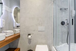 A modern bathroom with a glass shower enclosure, a wooden vanity with a sink, and a toilet. - Modern Romantic CIty Getaway (Warszawa)