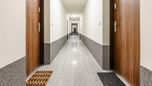 A hotel hallway with wooden doors, a tiled floor, and a doormat at the entrance. - Beautiful Seaview Flat in Stagadon Island (Łódź)