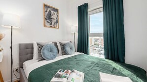 A hotel room with a bed, a window with curtains, a floor lamp, and a painting on the wall. - Beautiful Seaview Flat in Stagadon Island (Łódź)