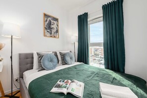 Ein Hotelzimmer mit Bett, einem Fenster mit Vorhängen, einer Stehlampe und einem Bild an der Wand.