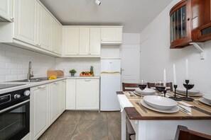Eine moderne Küche mit weißen Schränken, einem Backofen, einem Kühlschrank und einem Essbereich, der für eine Mahlzeit gedeckt ist.