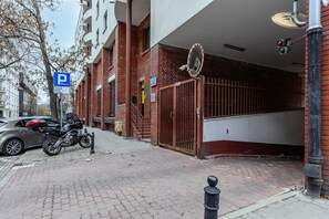 A parking area with a motorcycle parked, a gated entrance, and a building with a red brick facade. - Charming Warsaw Apartment for 6 (Warszawa 2)