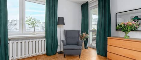 Una habitación con un radiador, un sillón gris, un aparador de madera y una lámpara de pie.