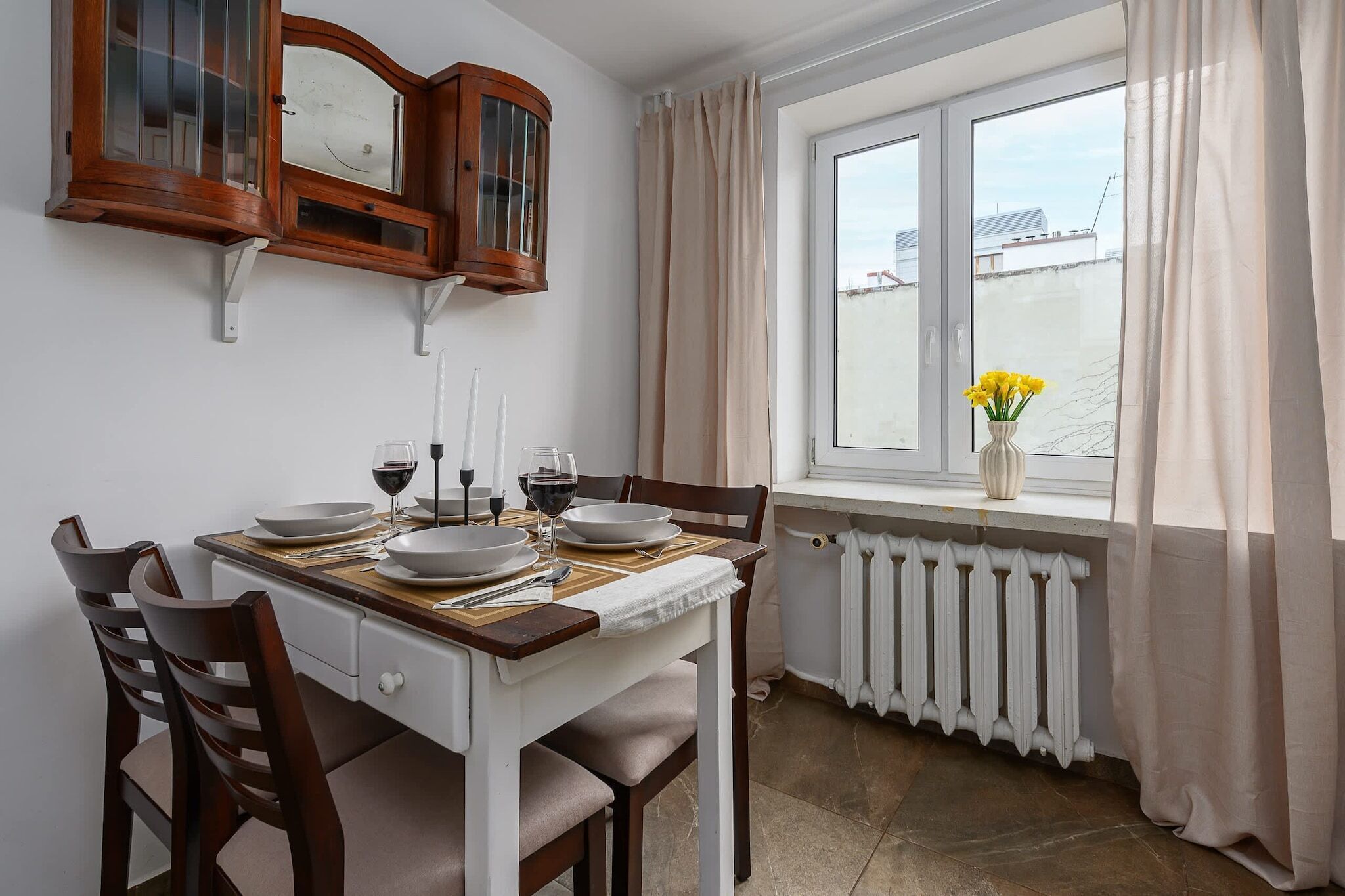 Ein Essbereich mit einem Tisch für vier Personen, einem Fenster mit Vorhängen und Blick auf ein Gebäude.