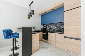 A modern kitchen with wooden cabinets, a blue backsplash, and a black countertop. - Luxurious Flat with magnificent sea view (Łódź)