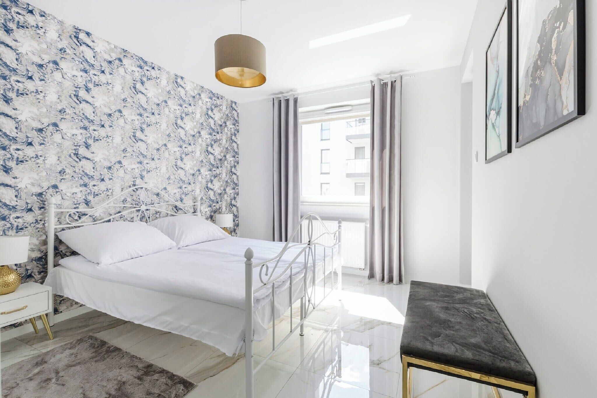 A modern bedroom with a bed, bedside table, lamp, and a view of the outside.