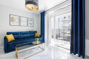 A modern living room with a blue sofa, a glass coffee table, and artwork on the wall. - Luxurious Flat with Magnificent City View (Łódź)