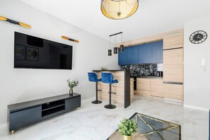 A modern living room with a flat-screen TV, a black entertainment unit, blue bar stools, and a glass coffee table. - Luxurious Flat with magnificent sea view (Łódź)