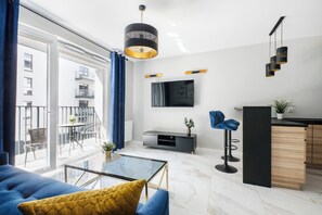 Un soggiorno moderno con un divano, un tavolino, una televisione e un balcone con vista sugli edifici.