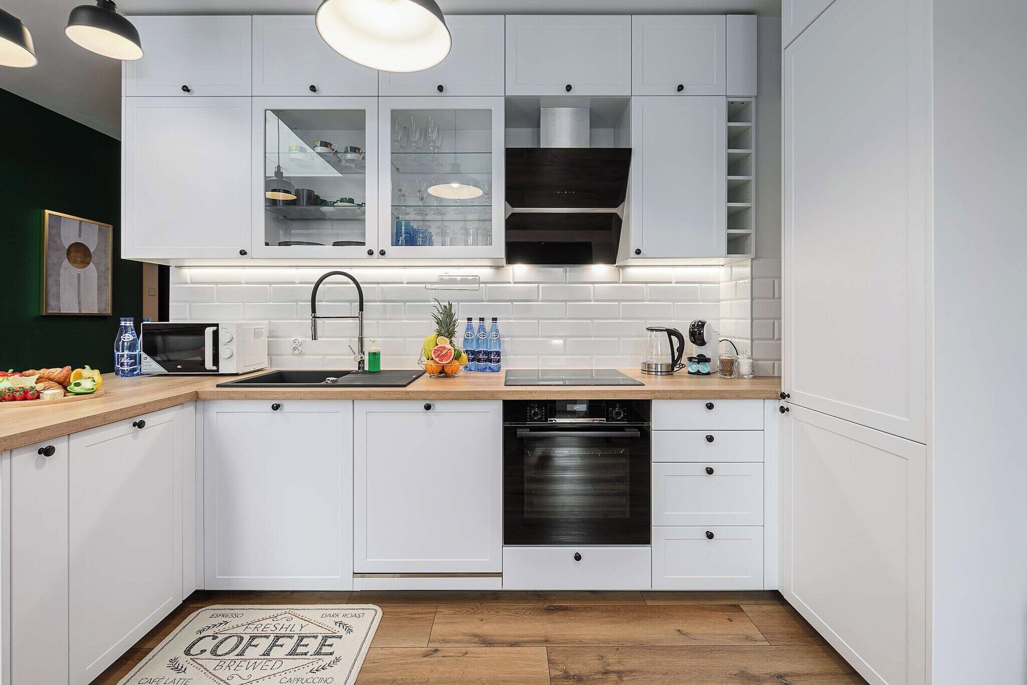 A modern kitchen with white cabinets, a stainless steel range hood, a dishwasher, and a countertop with a toaster and a fruit bowl.