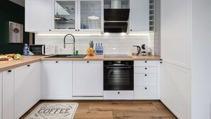 A modern kitchen with white cabinets, a stainless steel range hood, a dishwasher, and a countertop with a toaster and a fruit bowl. - Home near Piotrkowska Street (Łódź)